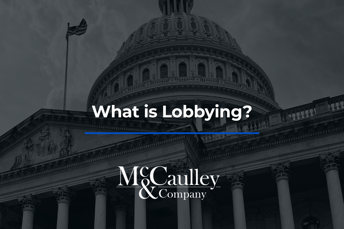 Darkened photo of the U.S. Capitol dome and columns with an American flag flying, overlaid with the text “What is Lobbying?” and the McCaulley & Company logo.