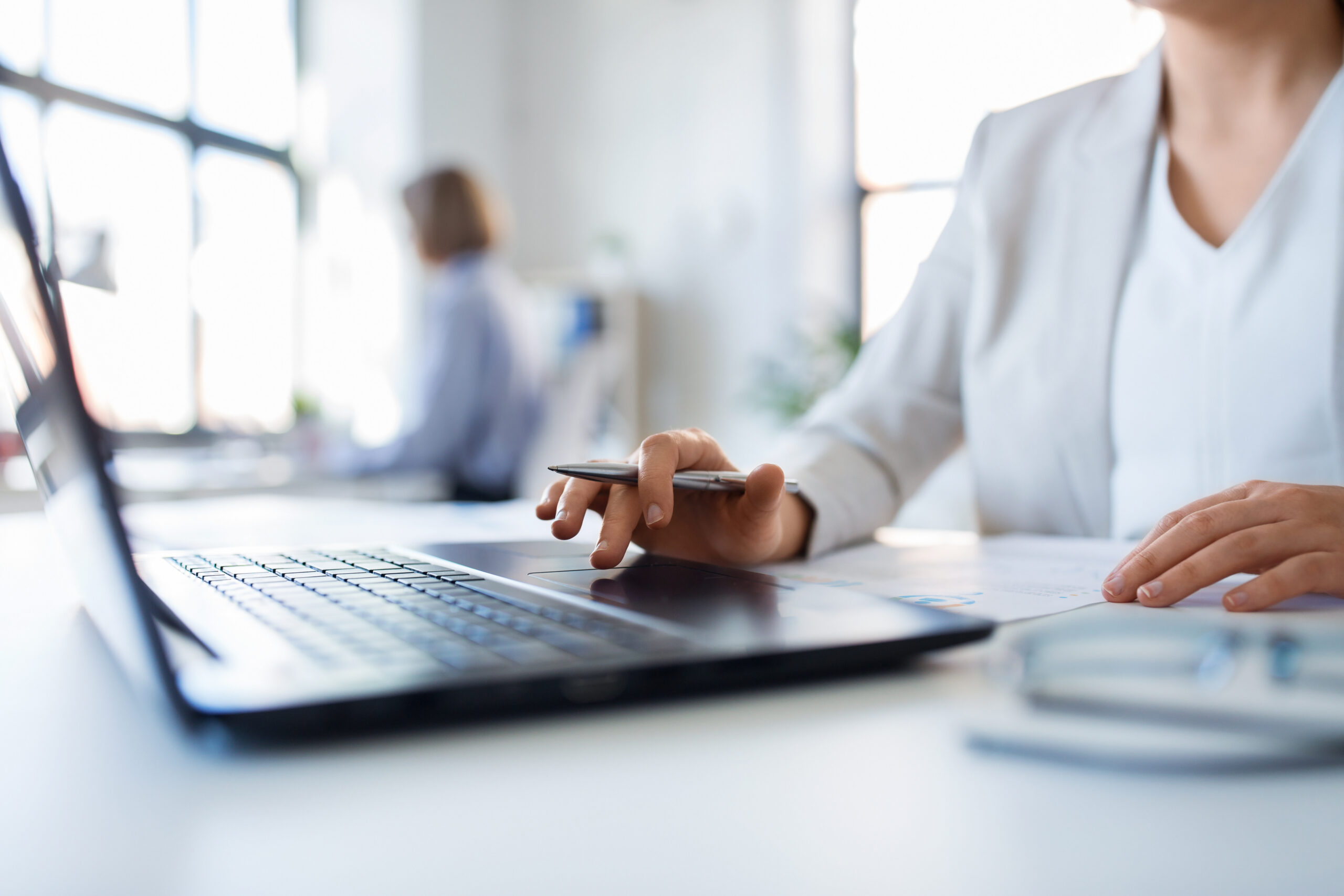Close-up of a professional in a white blazer working on a laptop at a desk, researching federal grant funding strategies.